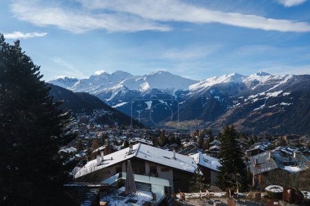 Malerisches Winterbergdorf mit schneebedeckten Dächern, Chalets und majestätischen Gipfeln in den europäischen Alpen, möglicherweise in der Schweiz, Österreich oder Frankreich.