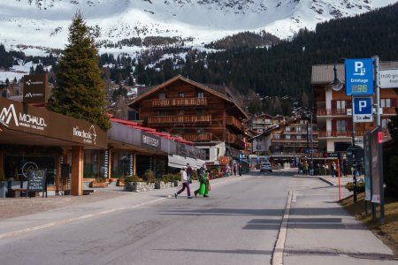 Téléchargez les photos : Scène de rue de montagne alpine dans une station de ski avec des personnes portant du matériel de ski, des bâtiments pittoresques de style chalet, des entreprises et une ambiance pittoresque. - en image libre de droit