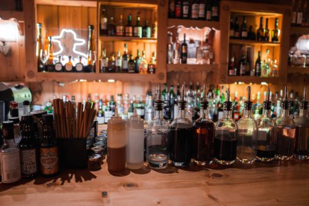 Photo for Bar counter stocked with colorful bottles, pour spouts, mixers, and straws, lit by a warm neon star sign. Cozy and rustic ambiance with no location data. - Royalty Free Image