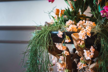 Un elegante arreglo de flores artificiales de melocotón en un estante de madera, rodeado de vegetación y toques de flores de color naranja y rosa. Perfecto para la decoración de interiores.