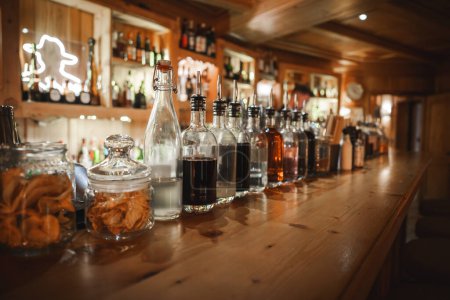 Inviting bar scene with neatly arranged jars and bottles on a wooden countertop. Warm lighting and cozy ambiance suggest a well stocked establishment.