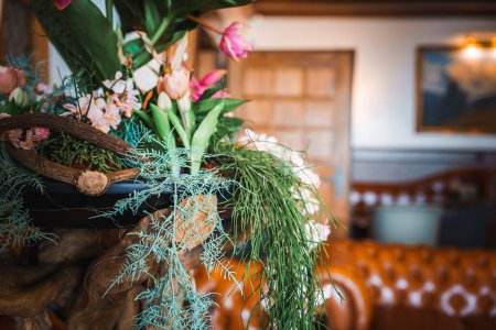 Fermer arrangement floral avec des tulipes roses dans une jardinière décorative en bois. Intérieur confortable avec canapé orange, image encadrée et ambiance chaleureuse, emplacement inconnu.