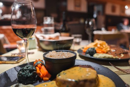 Elegante Tischdekoration mit Gourmet-Steakgerichten, Wein und Gemüse in einem gemütlichen unscharfen Restaurant-Interieur. Perfekt für gehobene Küche oder Lebensmittelpräsentation.