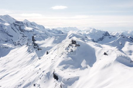 Breathtaking view of snow covered peaks at Murren ski resort, Switzerland. Pristine white snow blankets rugged terrain under clear sky, no skiers in sight. Grand mountain range extends into horizon.