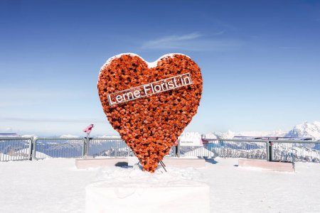 Téléchargez les photos : Grande structure en coeur ornée de fleurs rouges et bannière Lerne Floristin sur plate-forme d'observation enneigée à la station de ski Murren, Alpes suisses. Scène de journée ensoleillée. - en image libre de droit