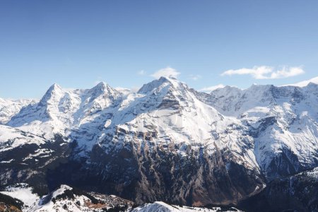 Photo for Experience the awe inspiring Swiss Alps with snow covered peaks and rugged slopes captured from the Murren ski resort. Majestic mountains under a clear blue sky create a dramatic alpine scene. - Royalty Free Image