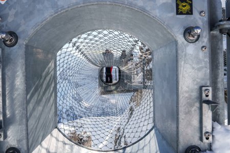 Explore a captivating perspective in a cylindrical tunnel structure with mesh exterior at Murren ski resort in Switzerland. Designed for safety, offering snowy mountain views.