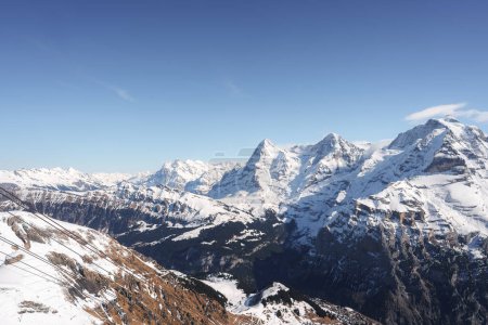Impresionante vista panorámica de los Alpes suizos cubiertos de nieve desde la estación de esquí de Murren. Majestuosas montañas, telesilla, pueblo abajo, cielos tranquilos. Ideal para actividades de invierno.