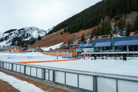 Foto de Los patinadores de hielo disfrutan de una animada pista de esquí al aire libre en la estación de esquí de Murren en Suiza. Edificios de estilo alpino y pintorescas laderas de montaña completan la escena invernal. - Imagen libre de derechos
