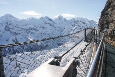 Breathtaking view of metal walkway at Murren ski resort, Switzerland. Snow covered mountains under clear blue skies, safe viewing platform for visitors.