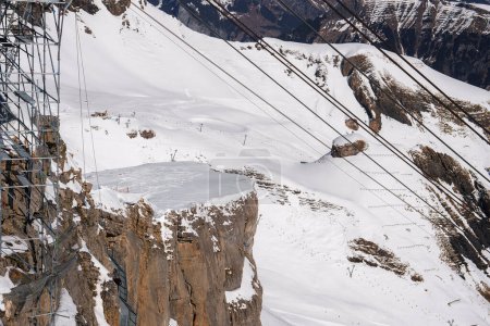 Foto de Escena de la estación de esquí alpino en Murren, Suiza. afloramiento rocoso con estructura metálica, pistas de esquí en la nieve, cuerpo congelado de agua, remontes que se extienden a través de pistas nevadas. - Imagen libre de derechos