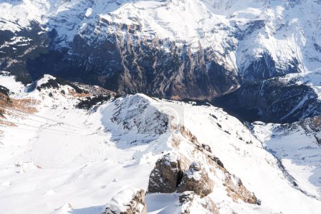 Breathtaking view of Murren ski resort in Switzerland. Snow covered peaks, ski tracks, village, Swiss Alps, light, and shadow create a serene winter scene.