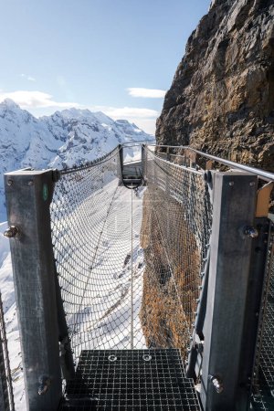 Photo for Explore a daring trail at Murren ski resort in Switzerland with a stunning image of a metal suspension bridge over a rocky chasm, surrounded by snow capped mountains. - Royalty Free Image