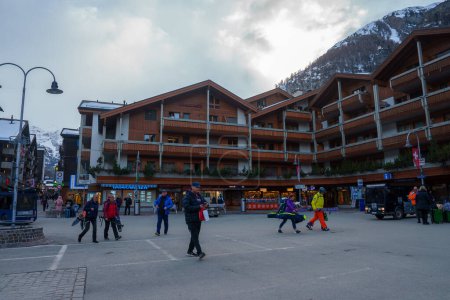 Photo for Lively street scene at Zermatt ski resort, Switzerland. People in ski attire walking by buildings with alpine architecture, mountain views, and eco friendly vibes. - Royalty Free Image