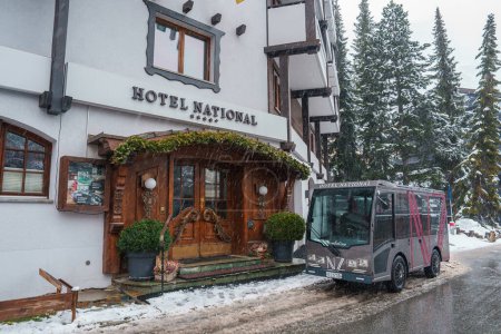Photo for Luxury hotel facade in Zermatt, Switzerland. White exterior with dark wood trim, alpine architecture. Entrance with green awning, snowy surroundings, shuttle bus. - Royalty Free Image