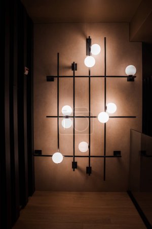 Modern luxury wall mounted light fixture with grid like pattern of black bars and white globes emitting warm light in interior of Zermatt ski resort, Switzerland.