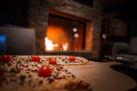 Leckere Pizza mit geschmolzenem Käse, Kirschtomaten und Kräutern auf einem Holzbrett in einem gemütlichen, gehobenen Ambiente mit Kamin in Zermatt, Schweiz.