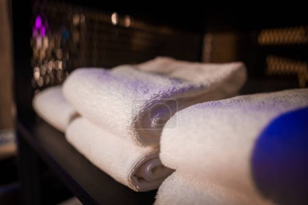 Luxurious white towels neatly rolled on a dark shelf in Zermatt, Switzerland. Fluffy and soft, perfect for hotel guests. Spa like ambiance with purple lighting.