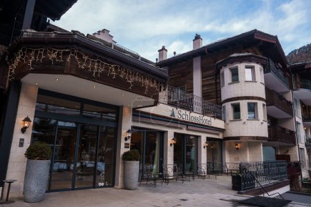 Foto de Lujoso hotel alpino en Zermatt, Suiza con arquitectura tradicional, balcones de madera y luces festivas. Acogedor y lujoso alojamiento con torreta única como estructura. - Imagen libre de derechos