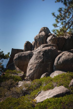 Natural rocky landscape under clear blue sky, featuring large weathered boulders and rugged vegetation. Bright, sunny day highlights rocky contours. Ideal for mountainous regions or national parks.