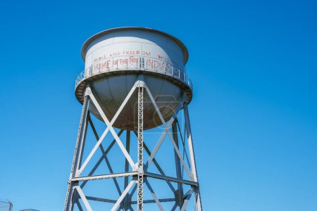 Photo for Tall white water tower with conical top, metal lattice beams, PEACE AND FREEDOM WELCOME HOME OF THE FREE INDIAN LAND message. Location Alcatraz Island, San Francisco, USA. - Royalty Free Image