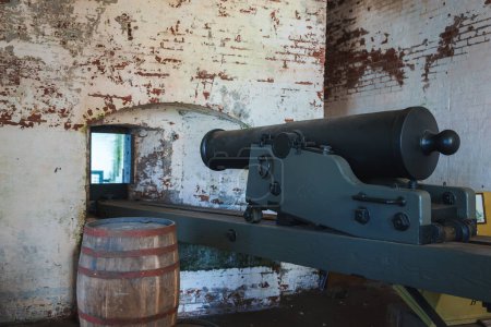 Explore an aged room at Alcatraz, San Francisco. An ancient cannon on a green carriage, worn walls with peeling paint, and a barrel enhance the historical vibe.