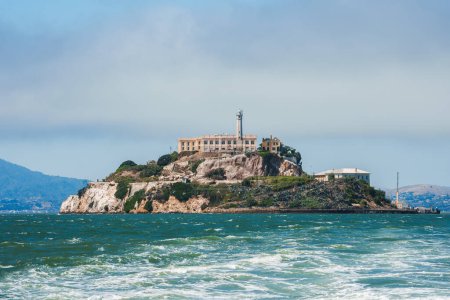 Erkunden Sie die robuste Insel Alcatraz in der Bucht von San Francisco, Kalifornien, USA. Ikonische Gebäude des Bundesgefängnisses und felsige Küsten vor einem teilweise bewölkten Himmel.