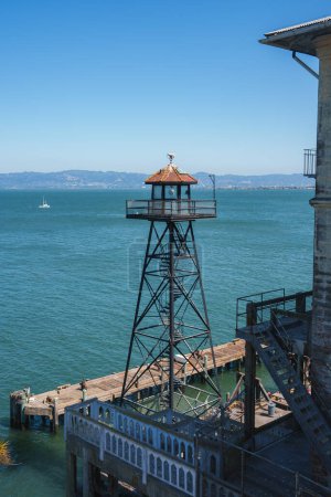 Blick vom Alcatraz-Gefängnis in San Francisco, USA. Ein Wachturm steht auf einem Pfeiler mit verwittertem Kuppeldach. Ein Boot schwimmt in der Bucht mit klarem Himmel.