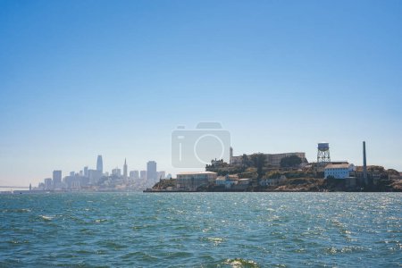Vista clara del día de la isla de Alcatraz desde el agua, mostrando la infame prisión con el paisaje urbano de San Francisco en el fondo. Ambiente sereno.