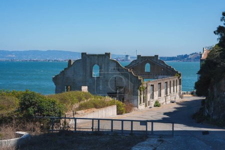 Erkunden Sie die Überreste eines historischen Gebäudes auf Alcatraz Island in der Bucht von San Francisco, USA. Verwitterte Mauern, blaues Wasser, entfernte Stadtsilhouette, die Wiedergewinnung der Natur.