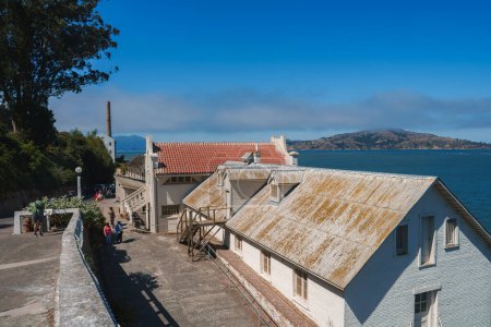 Téléchargez les photos : Explorez la prison historique d'Alcatraz à San Francisco, États-Unis. Bâtiments âgés avec murs blancs et toits rouillés sur fond de baie de San Francisco. - en image libre de droit