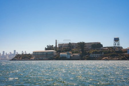 Blick auf die raue Insel Alcatraz in der Bucht von San Francisco, Kalifornien, USA. Zeigt Hauptzellhaus, Wachturm, abgehacktes Wasser und die Skyline der Stadt im Hintergrund.