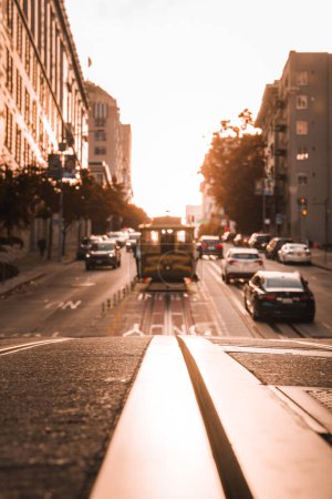 Iconic San Francisco cable car moves along a bustling street at sunset, bathed in warm golden light. Urban beauty captured from street level perspective.