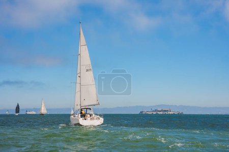 Foto de Navegando en la bahía de San Francisco con un yate blanco deslizándose a través de aguas verdes azules. Isla de Alcatraz visible en el fondo. Ideal para entusiastas de la vela. - Imagen libre de derechos