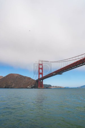 Iconic view of Golden Gate Bridge in San Francisco, CA. Towering red orange structure against a blue sky with clouds. Tranquil waters and Marin Headlands in background.