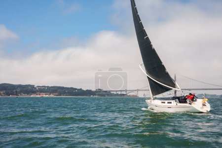 Foto de Yate de lujo navegando bajo San Francisco Oakland Bay Bridge en San Francisco Bay en un día tranquilo sin otros barcos cercanos, icónica vista de la ciudad en segundo plano. - Imagen libre de derechos