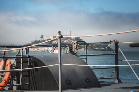 Nahaufnahme eines Bootsdecks mit maritimer Ausrüstung, das sich auf eine schwarze Struktur konzentriert. Golden Gate Bridge und Alcatraz Island im verschwommenen Hintergrund. Die Essenz der Bucht von San Francisco.