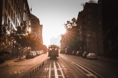 Photo for Scenic San Francisco street during sunset. Golden light, long shadows, iconic cable car, parked cars, bay windows, ornate facades. Serene urban landscape. - Royalty Free Image