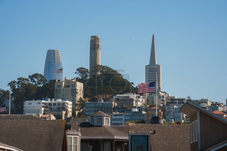 Szenische Ansicht von San Francisco präsentiert architektonische Stile, Wohngebäude, Hügel mit amerikanischer Flagge, Coit Tower, Transamerica Pyramide, klarer blauer Himmel.