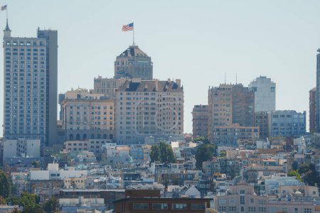 Daytime view of San Franciscos urban landscape. Iconic hilly terrain with buildings of varying heights. Dominant building with peaked roof and flag. Storied city architecture.