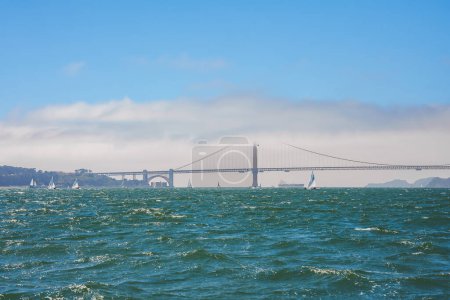 Gelassener Blick auf die Golden Gate Bridge von San Francisco, CA. Nebelige Brücke, Segelboote in der Bucht, klarer Himmel, Hügel in der Ferne ikonisches Stadtbild aus Natur und Technik.