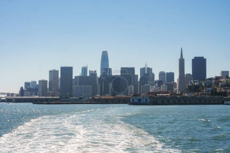 Daytime view of San Francisco skyline from the water, showing iconic buildings like Transamerica Pyramid and Salesforce Tower. Serene waterfront scene under clear blue sky.