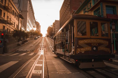 Photo for Iconic San Francisco cable car on steep incline at Van Ness Ave. and Market St. Golden sunlight casts long shadows on historic city street, no tourists. - Royalty Free Image