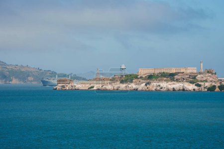 Una cautivadora vista de la isla de Alcatraz en la bahía de San Francisco. La infame ex prisión se destaca contra el horizonte, con un cielo nebuloso y colinas onduladas en el fondo.