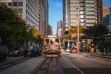 Photo for Classic San Francisco scene with iconic cable car on tracks under sunny skies. Wooden cable car and city buildings create bustling downtown atmosphere. - Royalty Free Image