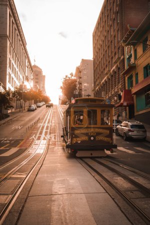 Photo for Iconic San Francisco cable car on steel tracks with warm sunlight, reflecting citys architecture. Powell Hyde line, tourists on board, serene street scene. - Royalty Free Image