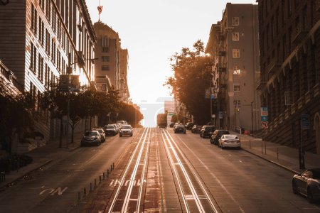 Photo for Serene sunset scene in San Francisco captures warm glow, long shadows, parked cars, tall buildings, cable car tracks, deserted streets, hilly terrain. - Royalty Free Image