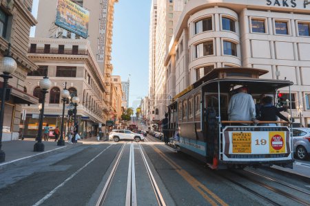 Photo for Iconic San Francisco cable car filled with passengers ascends a hilly street, surrounded by city architecture. Urban scene captures vibrant city life in the evening light. - Royalty Free Image