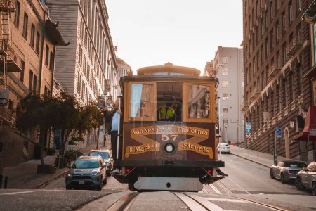 Téléchargez les photos : Le téléphérique classique de San Francisco monte la rue de la ville, étiqueté Van Ness Ave. California St. et Market St. Architecture iconique, éclairage chaleureux, scène pittoresque. - en image libre de droit
