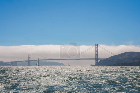 Ikonische Golden Gate Bridge in San Francisco, CA. Hoch aufragende, in Nebel gehüllte rot-orangefarbene Türme. Segelboote auf glitzernden Buchten, Hügel in der Ferne.